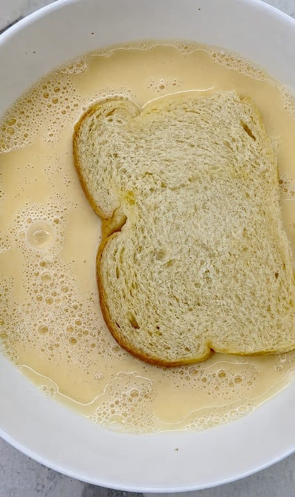 Soaking thick bread slices in homemade French toast batter before frying