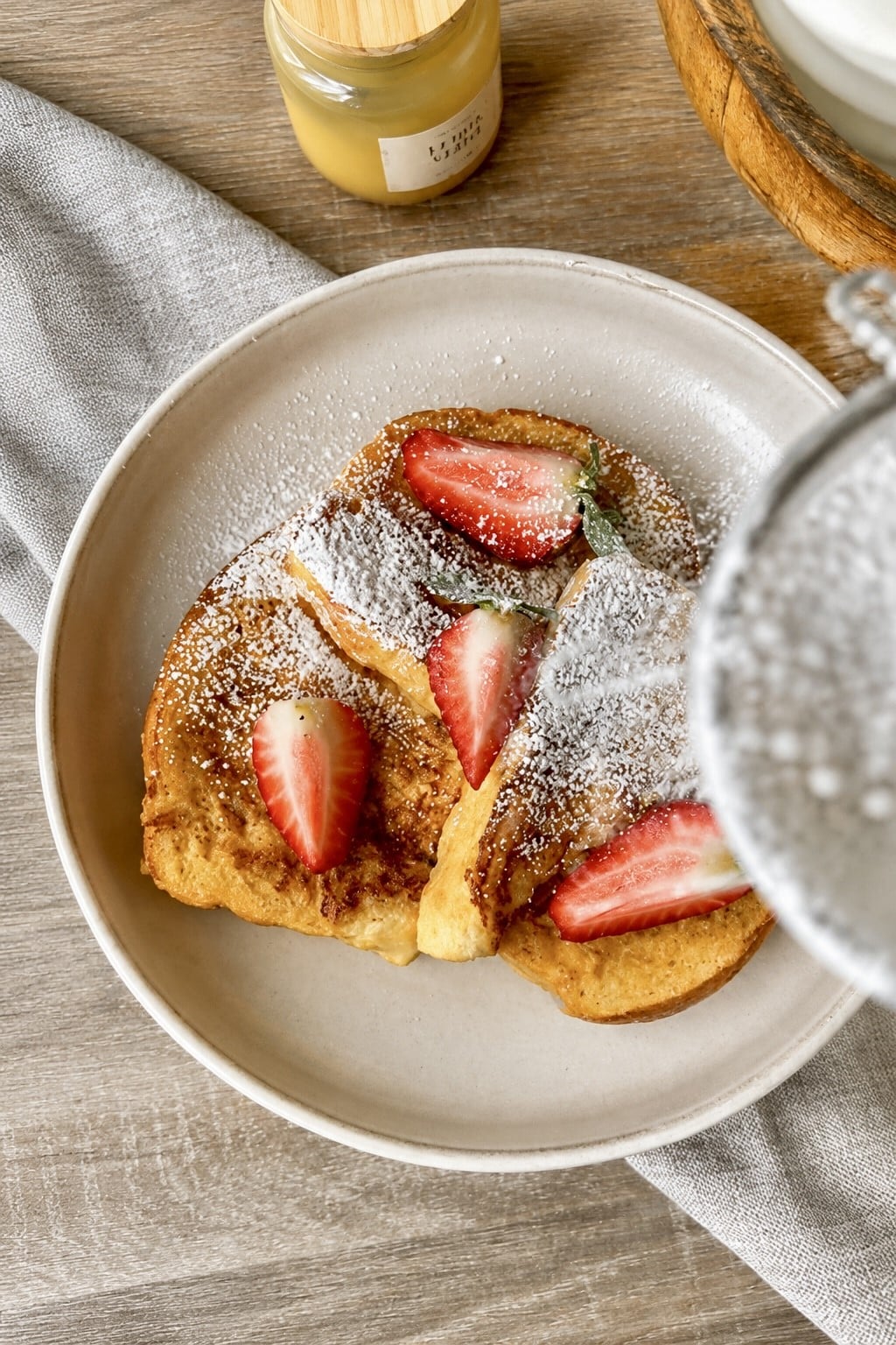 Thick-cut fluffy French toast stacked on a plate with fresh berries, powdered sugar, and maple syrup.
